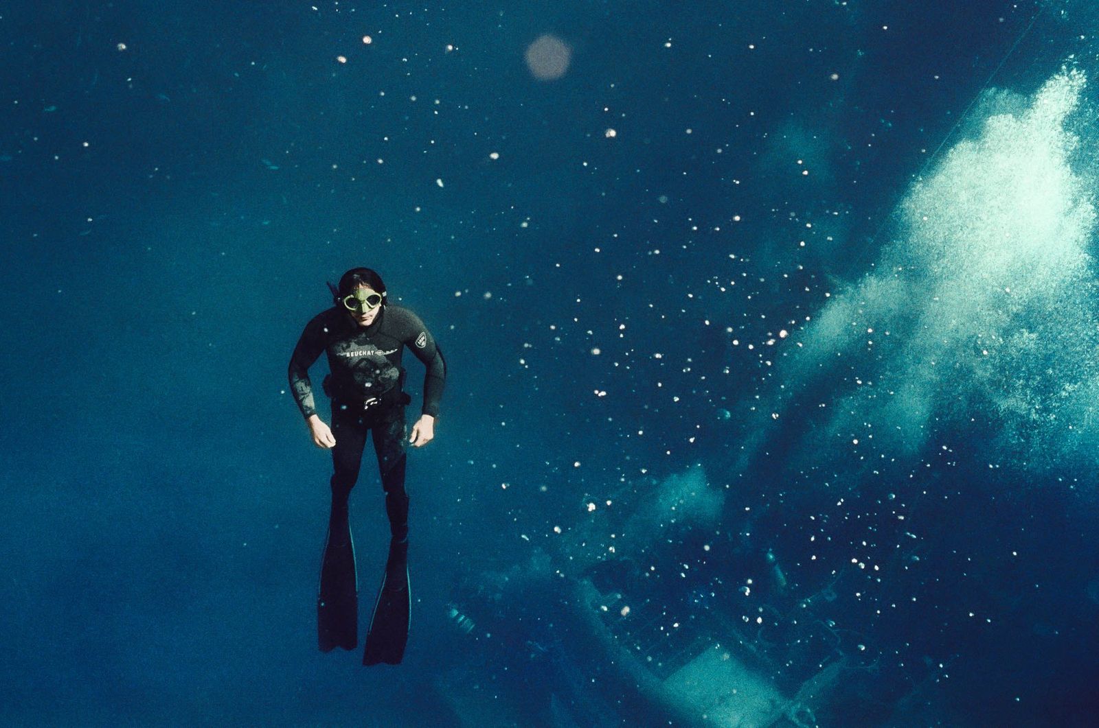 Freediver hanging in blue water among particles