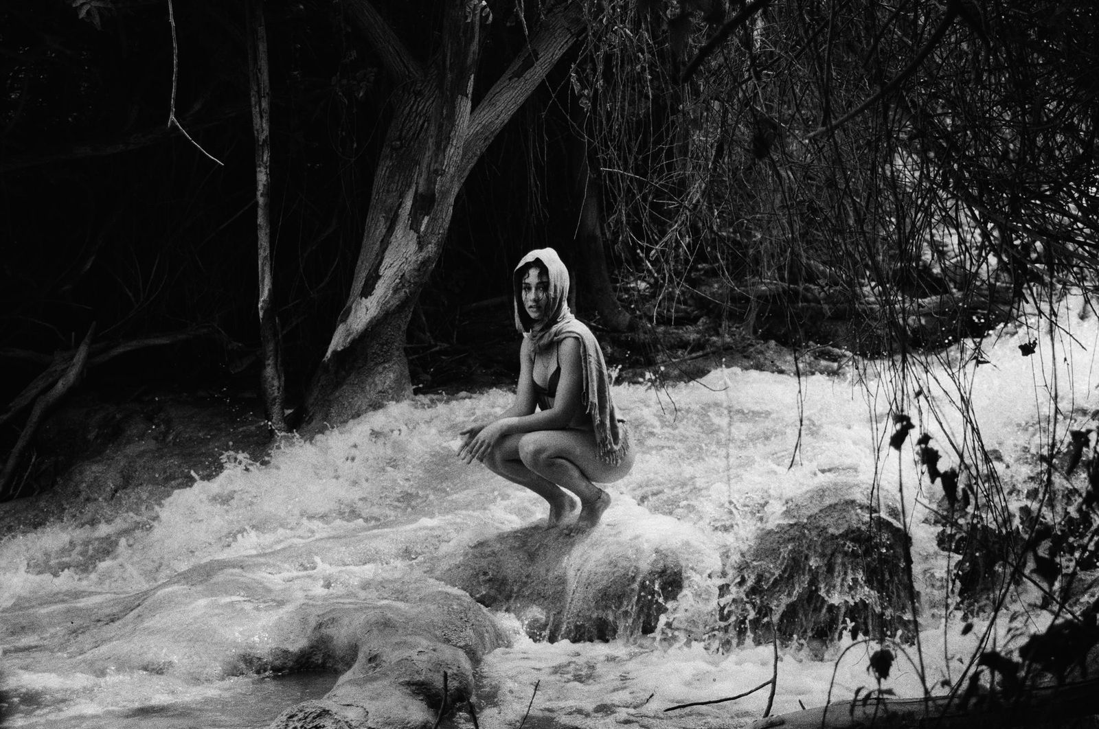 Black and white portrait of a woman crouched by a river