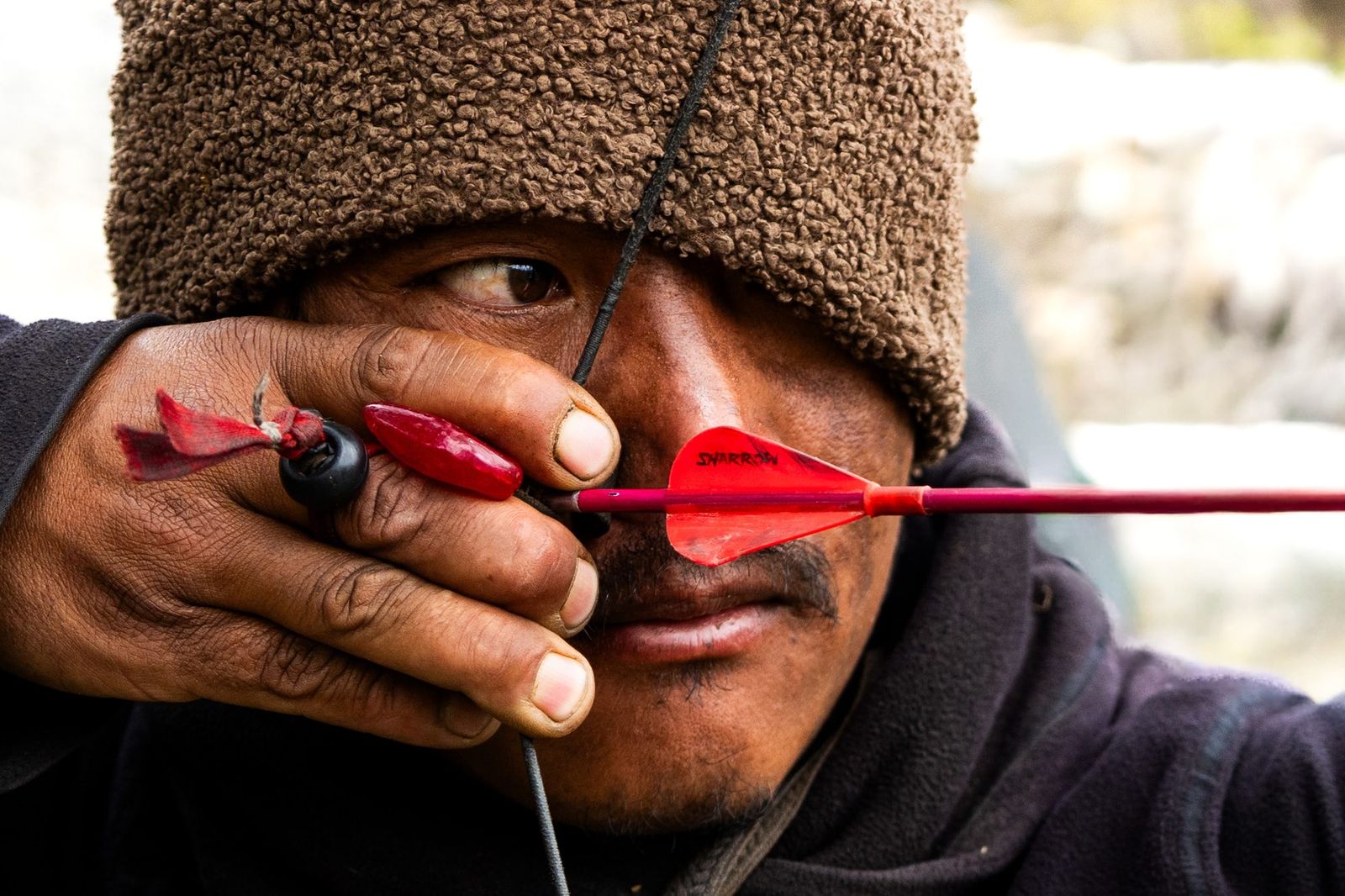 Close-up of an archer drawing a red-fletched arrow