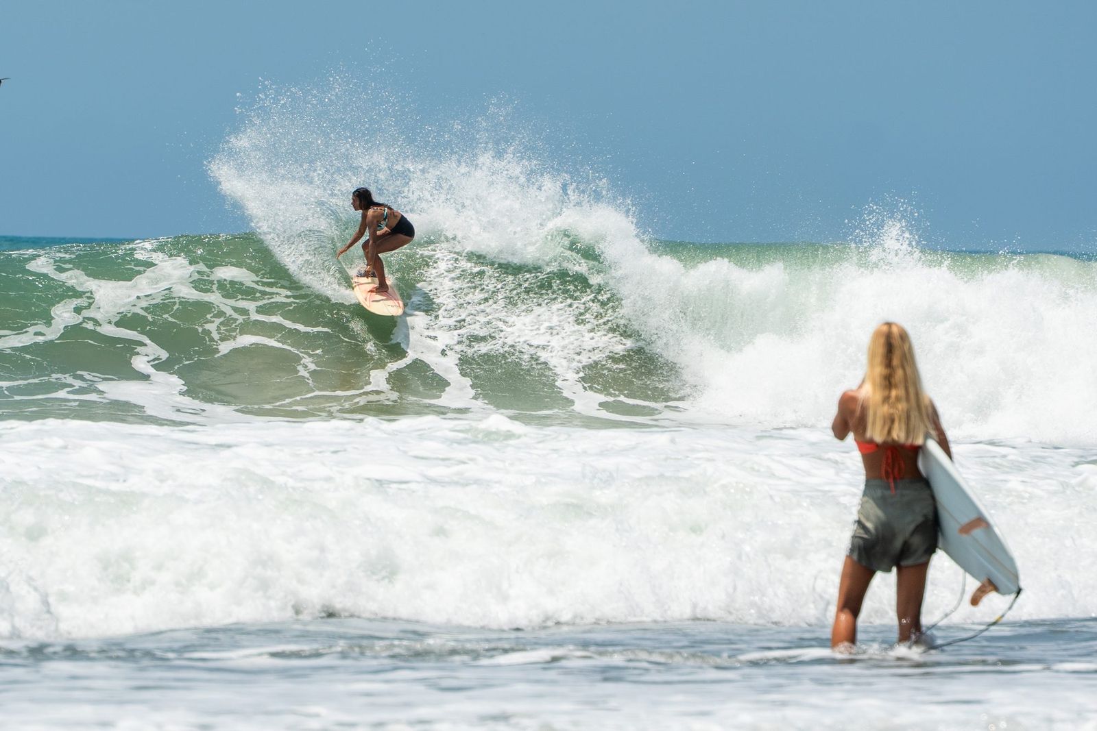 Surfer hitting the lip while another watches from the shallows