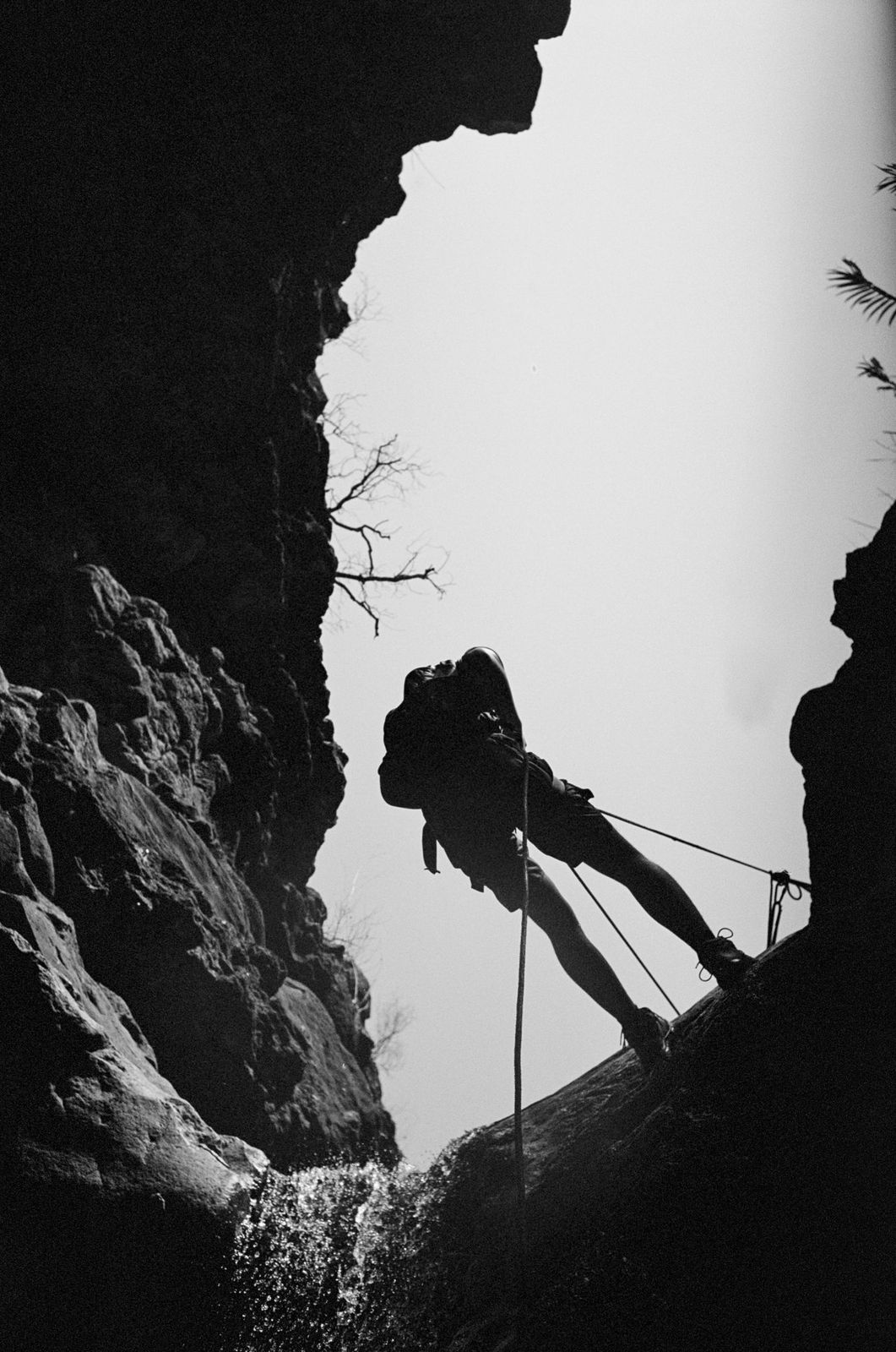 Black and white silhouette of a climber rappelling in a canyon